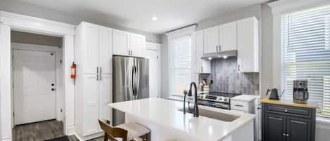 A modern kitchen with white cabinetry, a stainless steel refrigerator, a gas stove, and a coffee maker.