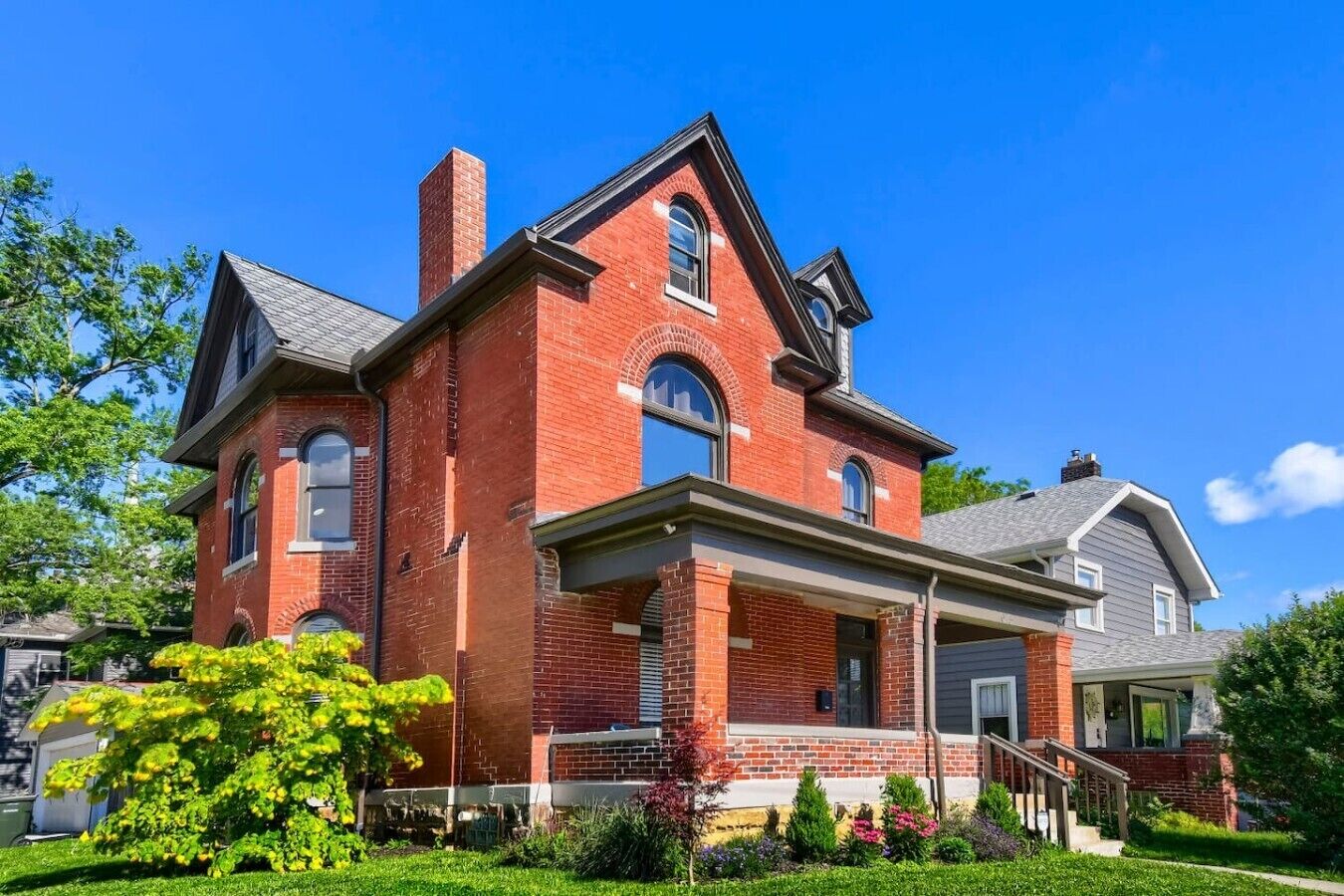 A two-story brick house with a front porch, a garage, and a well-maintained garden.