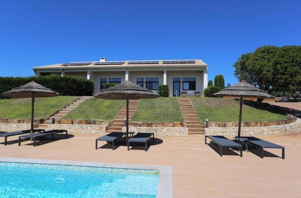 A hotel with a swimming pool, sun loungers, and a staircase leading to the entrance.