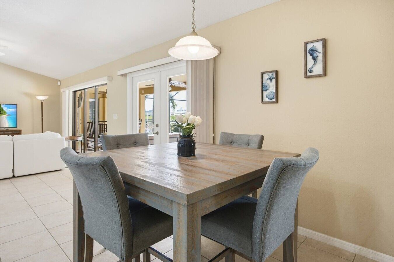 Un comedor con una mesa de madera, sillas tapizadas en gris, un jarrón con flores blancas y una obra de arte con caballitos de mar en la pared.