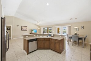 A modern kitchen with a dishwasher, wooden cabinets, and a dining area with a table and chairs. - Canal Home w/ Private Dock & Heated Pool, Hot Tub (Cape Coral)