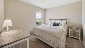 Ein Schlafzimmer mit einem Bett, einem Nachttisch, einer Lampe und einem Fenster mit Jalousien.