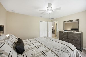 Un dormitorio con cama, cómoda, ventilador de techo y puerta que da a otra habitación.