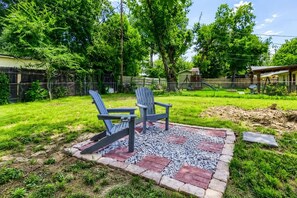 Un patio trasero con dos sillas Adirondack sobre un pavimento de ladrillo y grava, rodeado de césped y árboles.