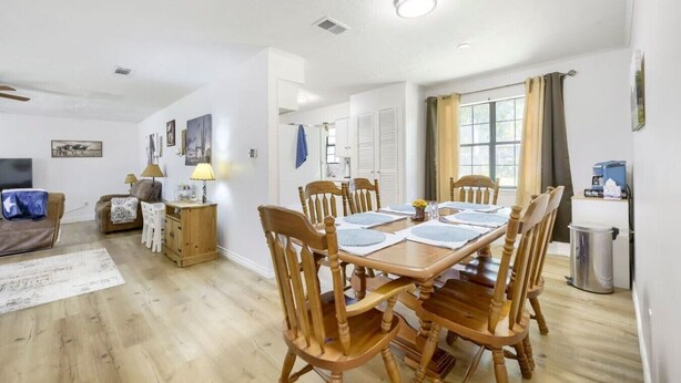 Uma sala de jantar com mesa de madeira posta para seis pessoas, rodeada por cadeiras de madeira.