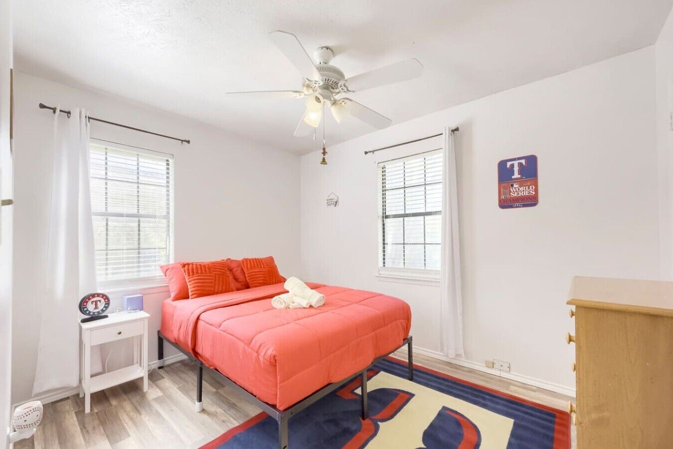 A bedroom with a bed, a nightstand, a dresser, a ceiling fan, and a window with blinds.