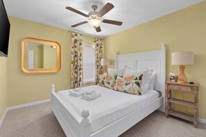 A bedroom with a white bed, a ceiling fan, a bedside table with a lamp, and a mirror on the wall. - Family Getaway with Pool and Game Room (Davenport)