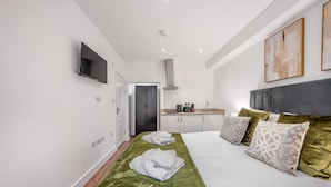 A hotel room with a bed, a flat-screen TV, a kitchenette, and a door leading to a bathroom. - Standard Studio With Terrace In Knightsbridge (London)