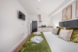 A hotel room with a bed, a flat-screen TV, a kitchenette, and a door leading to a bathroom. - Standard Studio With Terrace In Knightsbridge (London)