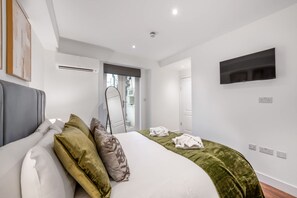 A modern hotel room with a large bed, a flat-screen TV mounted on the wall, and a window with a view of the city. - Standard Studio With Terrace In Knightsbridge (London)
