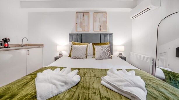 A hotel room with a bed, bedside tables, a nightstand, a mirror, an air conditioning unit, and a small kitchenette. - Standard Studio With Terrace In Knightsbridge (London)