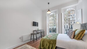 Ein Schlafzimmer mit einem Bett, einem Schreibtisch, zwei Stühlen, einer Heizung und einem Fernseher an der Wand.