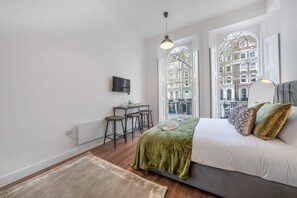 Ein Schlafzimmer mit einem Bett, einem Schreibtisch, zwei Stühlen, einer Heizung und einem Fernseher an der Wand.