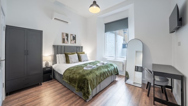 Een moderne slaapkamer met een bed, een bureau, een kledingkast en een groot raam.