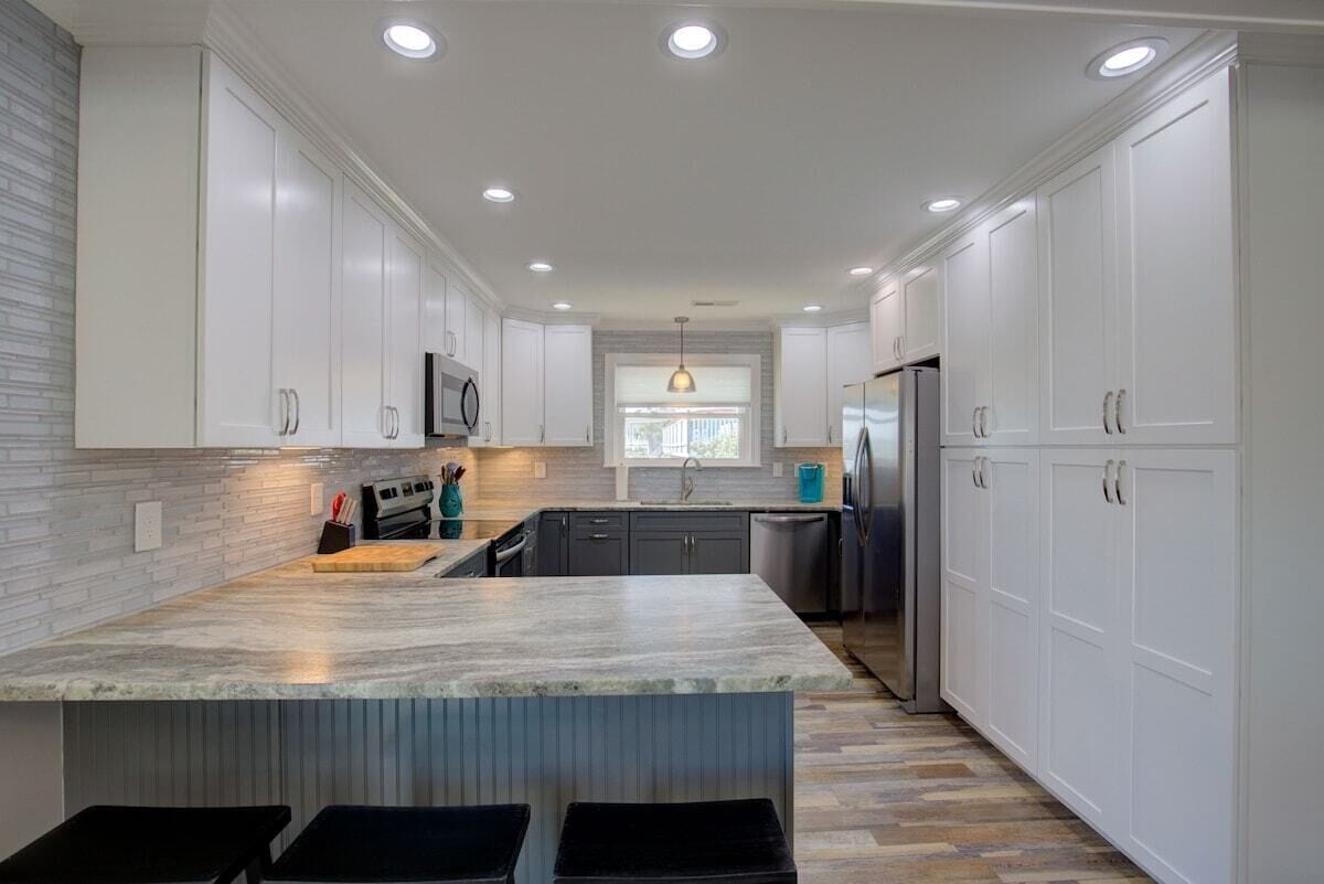 A modern kitchen with white cabinetry, a marble island, and recessed ceiling lights.