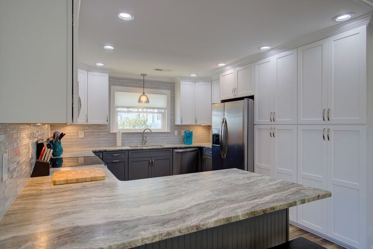 A modern kitchen with white cabinets, a granite countertop, and a stainless steel refrigerator.