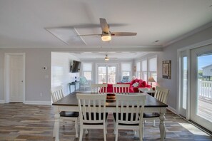 A dining area with a table, chairs, ceiling fans, and large windows. - Canalfront dock, boat ramp and hot tub (North Topsail Beach)