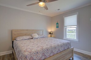 A bedroom with a wooden bed, a ceiling fan, a nightstand with a lamp, a window with blinds, and a wall-mounted decoration. - Canalfront dock, boat ramp and hot tub (North Topsail Beach)