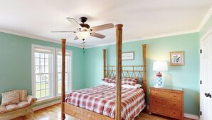A four-poster bed with a ceiling fan, a wicker sofa, a nightstand with a lamp, and a framed picture on the wall. - Canalfront dock with hot tub and views (North Topsail Beach)