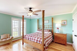 Ein Bett mit Baldachin, ein Deckenventilator, eine Korbschaukel, ein Nachttisch mit Lampe und ein gerahmtes Bild an der Wand.