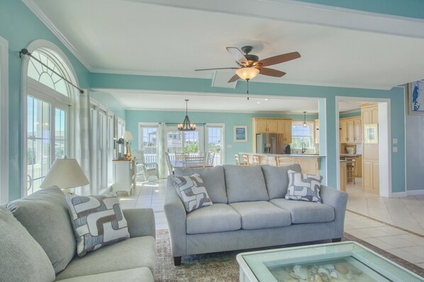 A spacious living room with a grey sofa, a coffee table, and a view of the kitchen and dining area. - Canalfront dock with hot tub and views (North Topsail Beach)