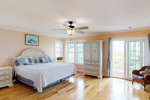 A bedroom with a bed, a nightstand, a dresser, a chair, a ceiling fan, and a large window. - Canalfront dock with hot tub and views (North Topsail Beach)