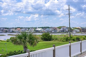 A residential area with houses along a waterfront, a grassy area with a palm tree, and a white fence. - Canalfront dock with hot tub and views (North Topsail Beach)