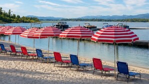 A beach with rows of striped umbrellas and beach chairs, a calm lake, and distant mountains. - Tamarack Resort Village Ski In Ski Out Condo - Year Round Resort (Donnelly)