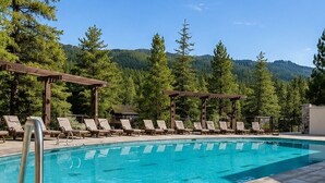 A pool with lounge chairs and a pergola, surrounded by trees and mountains. - Tamarack Resort Village Ski In Ski Out Condo - Year Round Resort (Donnelly)