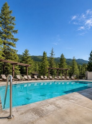 Ein Pool mit Liegestühlen und einer Pergola, umgeben von Bäumen und Bergen.