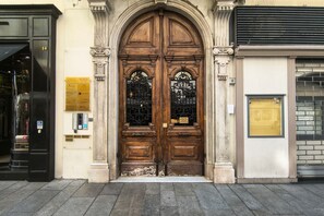 A double wooden door with a plaque, a black door to the left, and a brick wall to the right. - Il Rifugio della Riviera · Attic Studio (Sanremo)