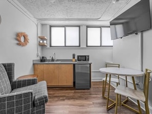 Een compacte keuken met een magnetron, spoelbak en vaatwasser. Er is een eethoek met een witte tafel en stoelen.