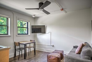 Ein Zimmer mit Deckenventilator, einem an der Wand befestigten Flachbildfernseher, einem Holztisch mit Stühlen und einem grauen Sofa mit Kissen.