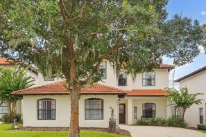 A two-story house with a tiled roof, a large tree in front, and a well-maintained lawn. - Cozy 5BD 3,5BA Clermont Villa/Heated Pool/Parks (Clermont)