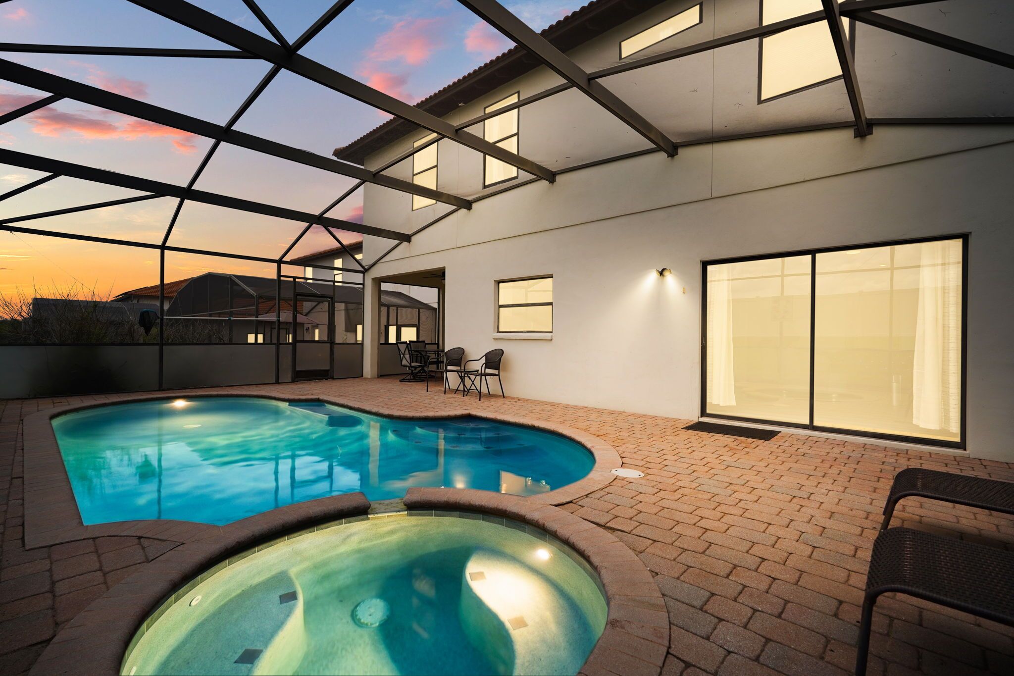 A swimming pool with a glass ceiling, a patio area with chairs, and a large window.