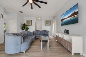 A modern living room with a sectional sofa, a glass coffee table, a white console table, and a mounted TV. - Cozy 5BD 3,5BA Clermont Villa/Heated Pool/Parks (Clermont)
