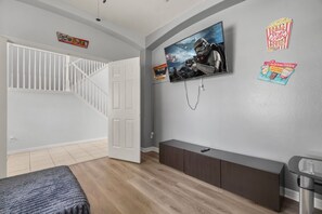 A modern living room with a staircase, a flat-screen TV mounted on the wall, and a dark wood cabinet. - Cozy 5BD 3,5BA Clermont Villa/Heated Pool/Parks (Clermont)