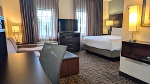 Una camera d'albergo con un letto, una scrivania, una sedia, una televisione e un comò.