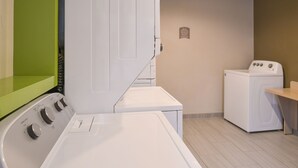 Una lavanderia con una lavatrice e un'asciugatrice Whirlpool, uno scaffale verde e una parete beige con una targa.
