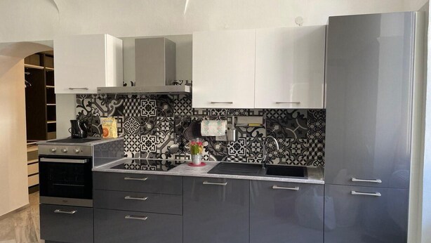 Eine moderne Küche mit dunklen Schränken, einem Edelstahl-Kühlschrank und Fliesen mit Muster.