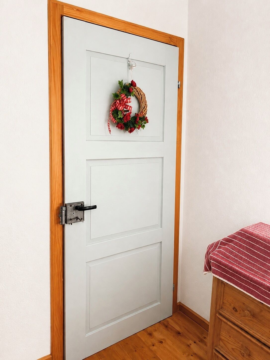 Una puerta blanca con marco de madera, un picaporte negro y un lazo rojo y blanco a cuadros.