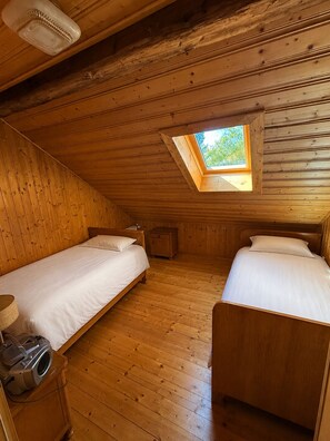 Una habitación pequeña y acogedora con dos camas individuales, un tragaluz, paredes de madera y suelo de madera.