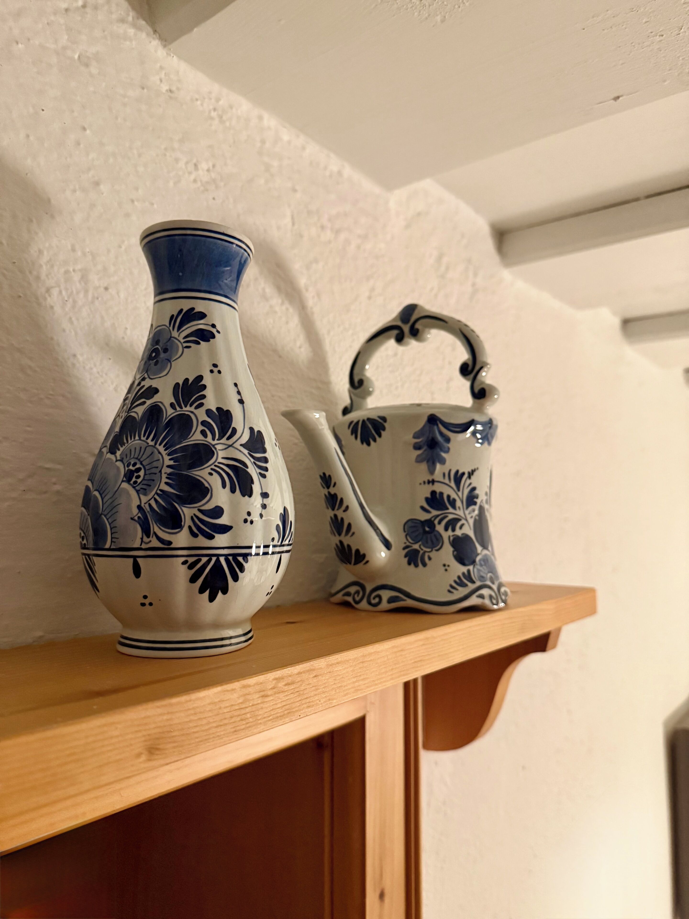 Une étagère en bois sur laquelle sont posés un vase blanc et un pichet blanc orné de motifs floraux bleus.