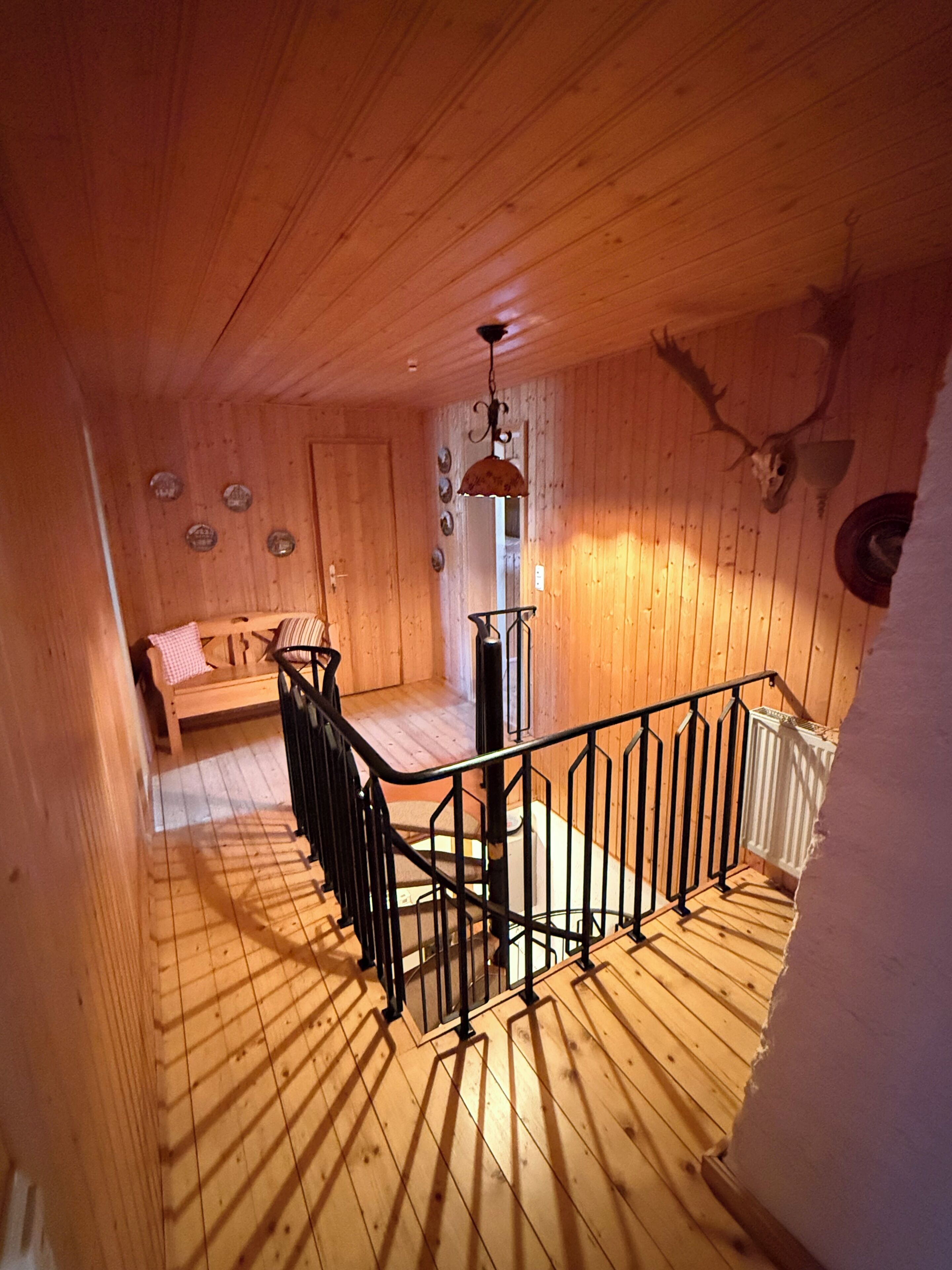 Interior de madera con una escalera, un banco y una calavera de ciervo montada en la pared.