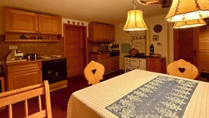 A kitchen with wooden cabinets, a stove, and a table with a patterned tablecloth. - Joslheisl Breitenberg (Breitenberg)