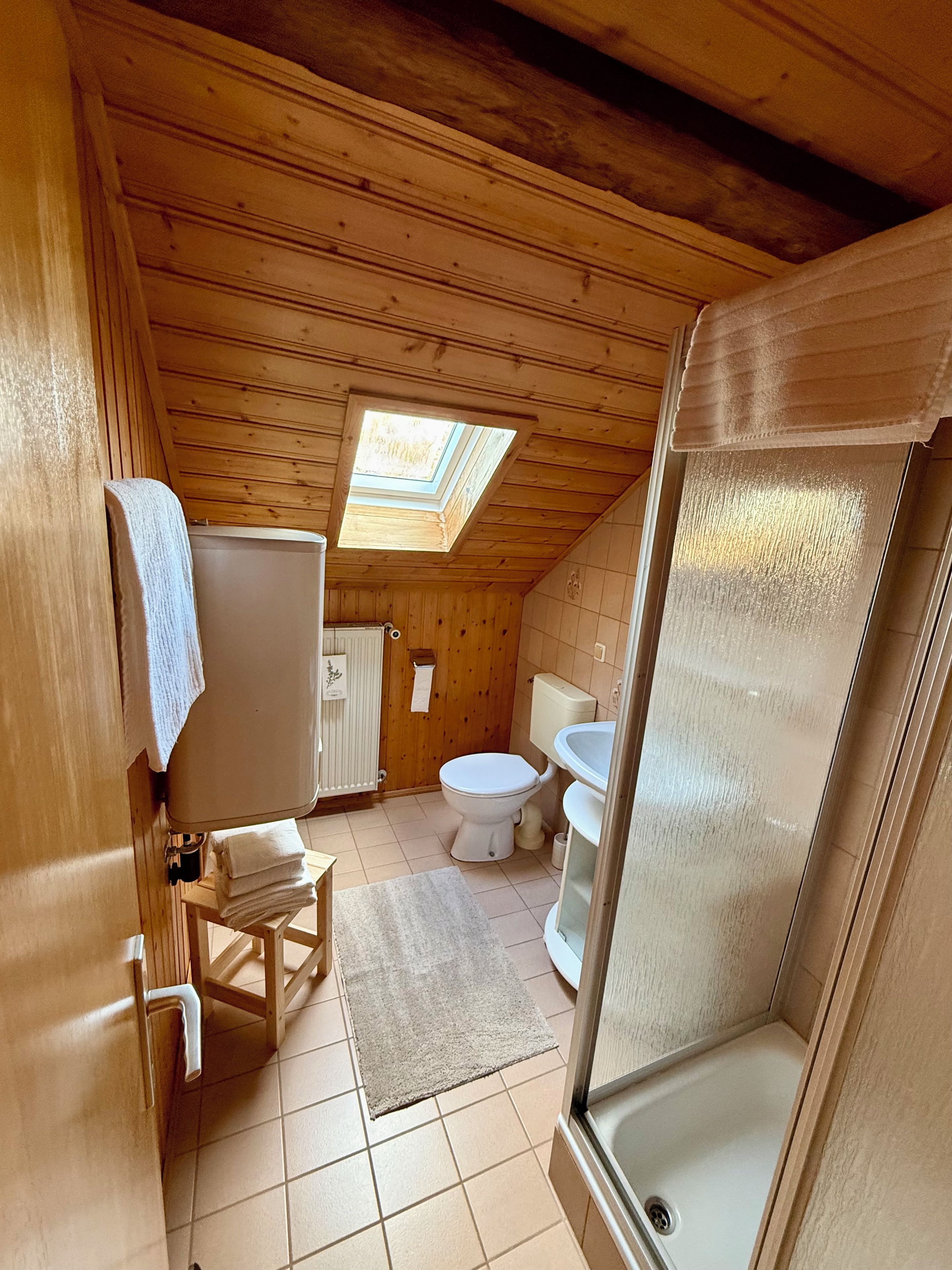 Ein kleines Badezimmer mit Holzverkleidung, einem Oberlicht, einer Toilette, einer Dusche und einem Handtuchhalter.