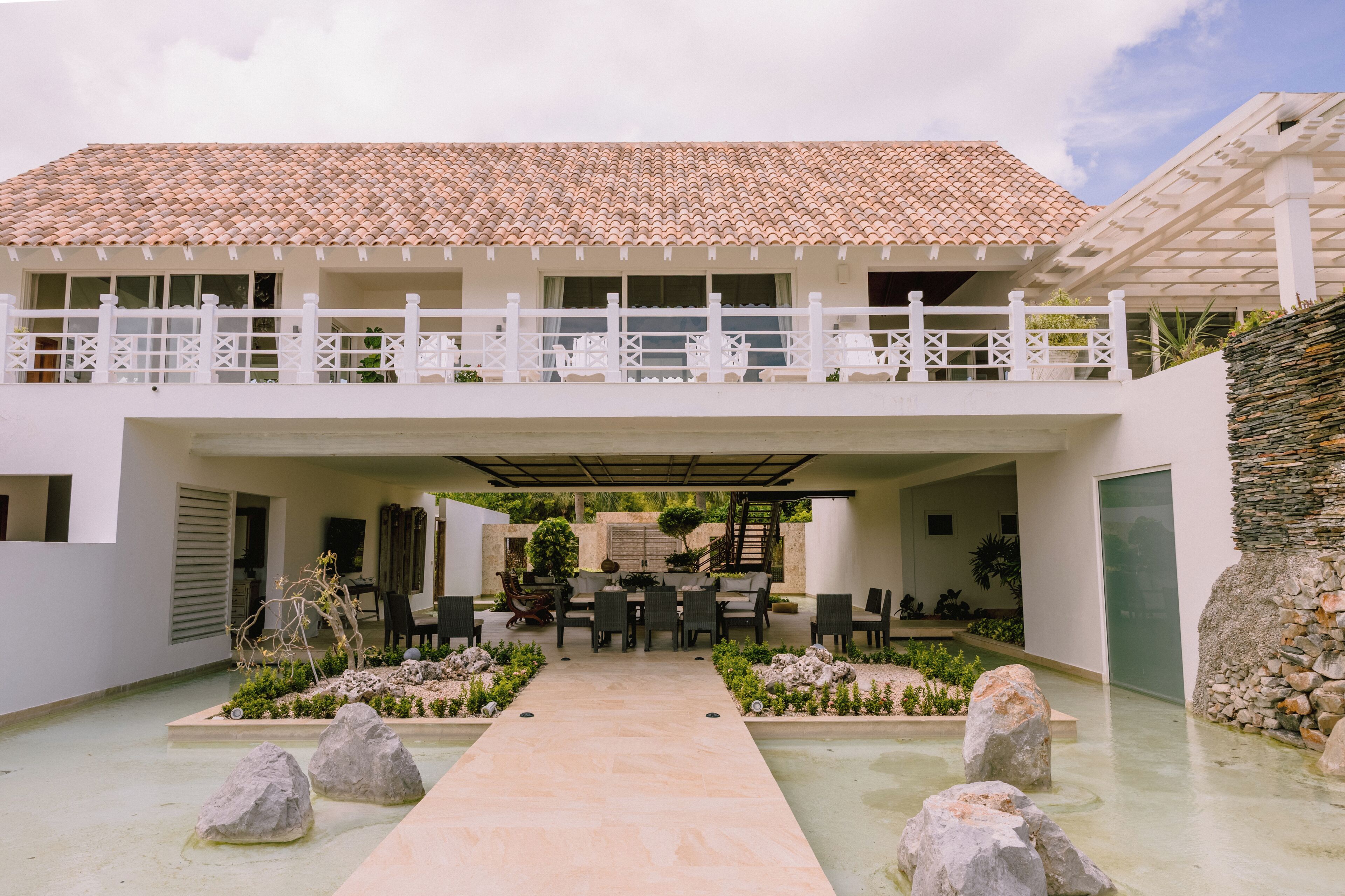 A modern building with a tiled roof, a covered patio area with outdoor furniture, and a stone pathway leading to the entrance.