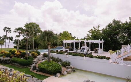 A pool area with a white pergola, palm trees, and a stone pathway.