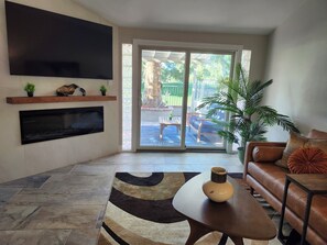 A living room with a flat-screen TV, a sofa, a coffee table, and a view of the outdoors. - Beautiful home on the 8th hole of LV Country Club! (Las Vegas)