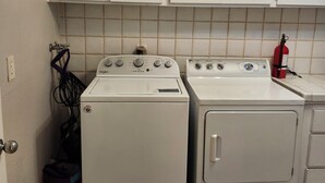 Ein Waschraum mit zwei weißen Whirlpool Waschmaschinen und Trocknern, einer gefliesten Spritzschutzwand und einem Feuerlöscher auf der Arbeitsfläche.